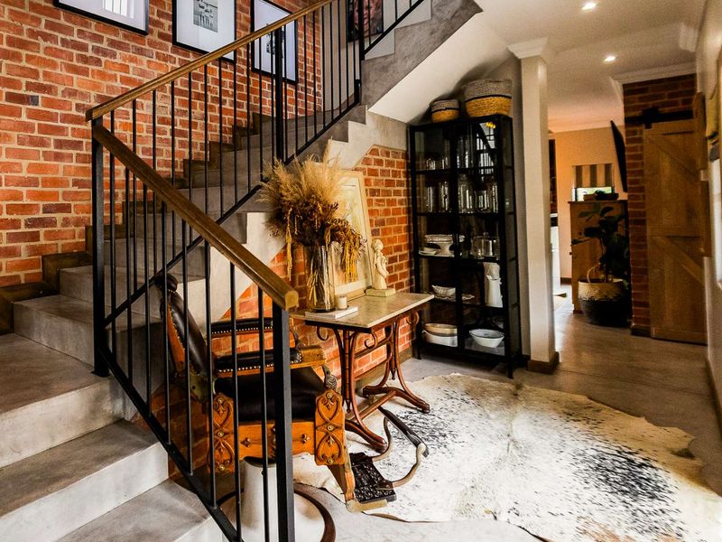 Welcoming entrance hall featuring a striking exposed brick wall, polished concrete flooring, and a modern concrete staircase with a sleek metal balustrade.