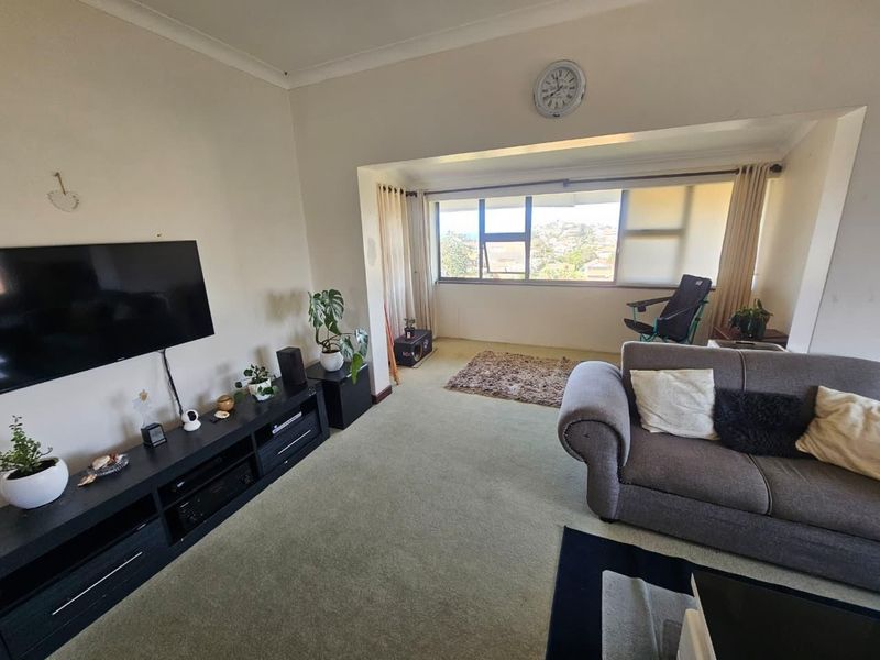 A living room featuring large windows with natural light, carpeted flooring, and coving detail, offering a comfortable space with potential for cosmetic updates.