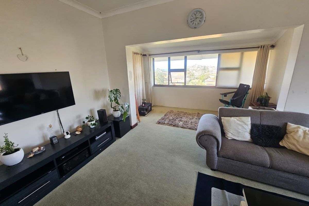 A living room featuring large windows with natural light, carpeted flooring, and coving detail, offering a comfortable space with potential for cosmetic updates.