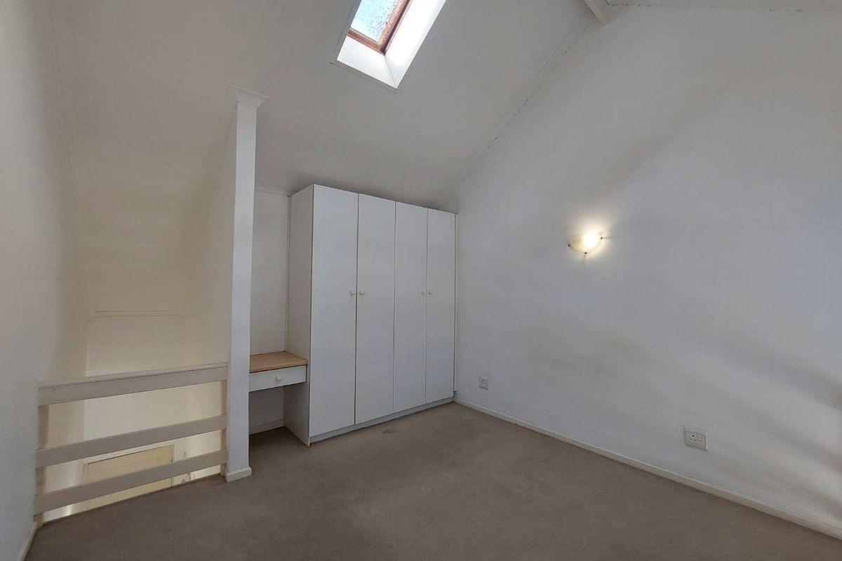 An attic-style bedroom featuring a skylight, built-in wardrobe with integrated desk space, and neutral carpet flooring.