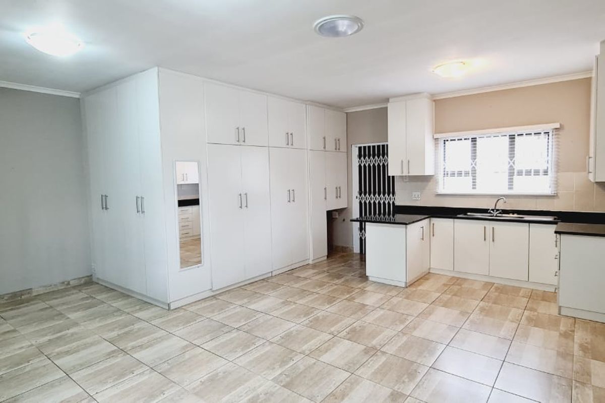 An open-plan living and kitchen area featuring extensive built-in white cabinetry, tiled flooring, and a functional kitchen layout with a sink and window.