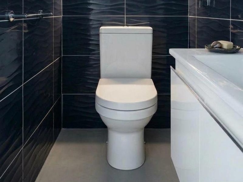 Modern bathroom featuring a white toilet, sleek vanity with integrated sink, and striking dark textured wall tiles.