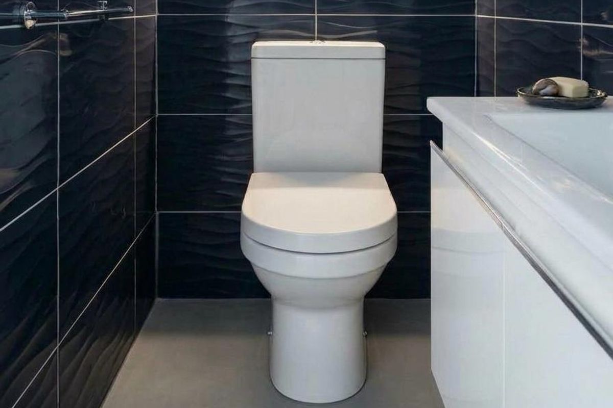 Modern bathroom featuring a white toilet, sleek vanity with integrated sink, and striking dark textured wall tiles.