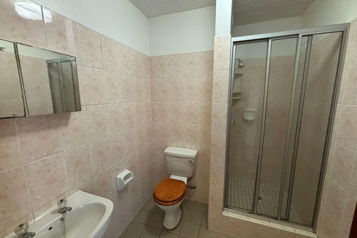 A functional bathroom featuring a shower enclosure, pedestal basin, and toilet with neutral wall tiling.