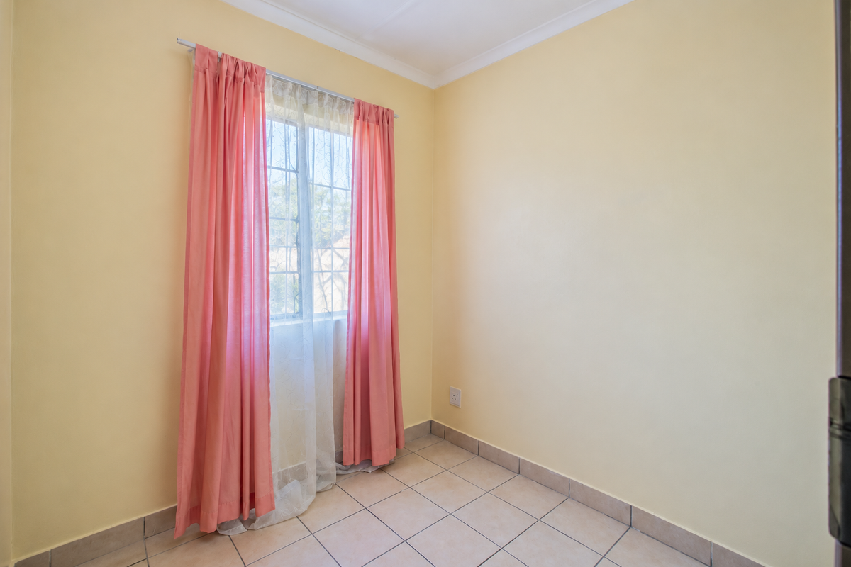 A bright, empty bedroom featuring neutral walls, tiled flooring, and a window with security bars, offering a clean canvas for personalization.