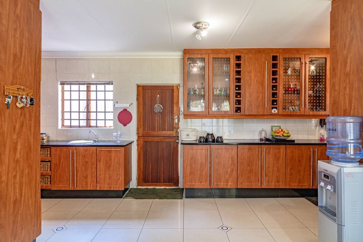 A functional kitchen featuring warm-toned wooden cabinetry, tiled flooring, a stainless steel sink, and a tiled backsplash with a secure exterior door.