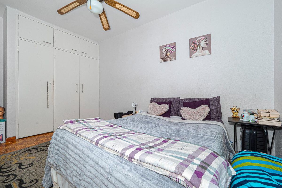 A bedroom featuring built-in wardrobes and a ceiling fan, with parquet flooring and neutral wall finishes.