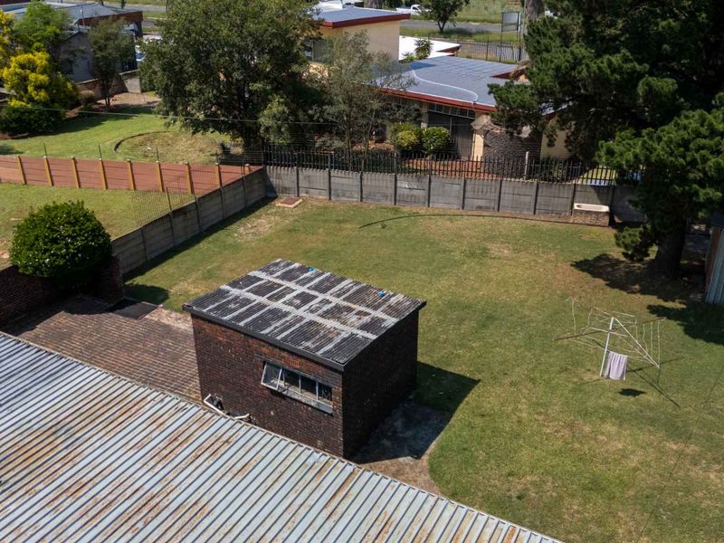 Aerial view of a spacious backyard featuring a brick outbuilding with a corrugated metal roof and perimeter boundary walling.