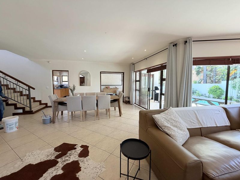 Spacious open-plan living and dining area featuring tiled floors, a staircase with a metal balustrade, and large sliding doors opening to the patio.