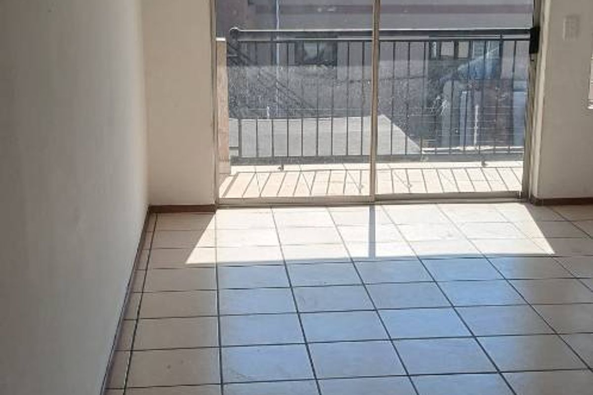 An empty living room featuring tiled flooring and a sliding glass door providing access to a balcony.