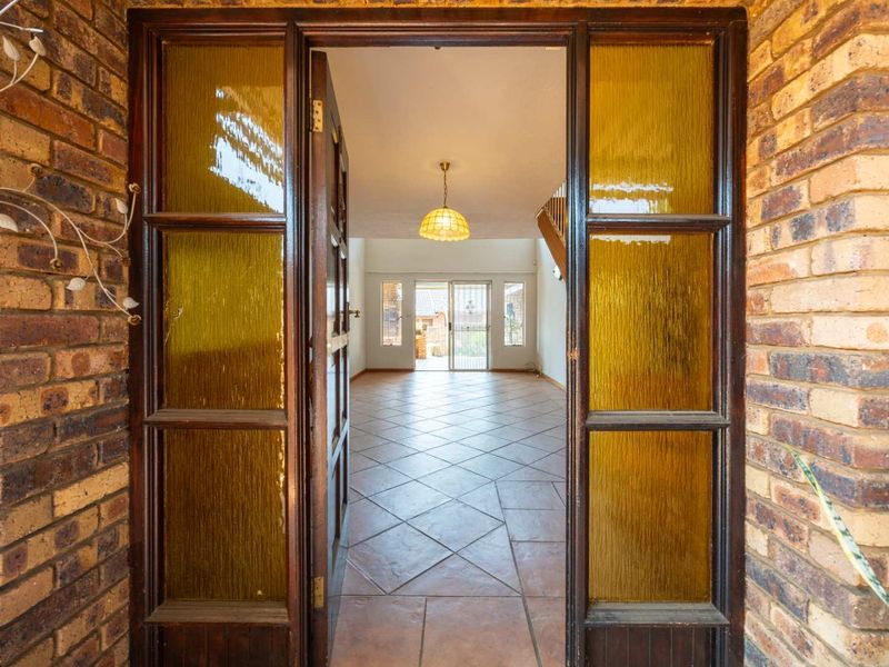 Entrance foyer featuring tiled flooring, exposed brickwork, and a timber-framed glass door leading into an open-plan living area.