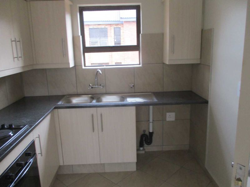 A functional kitchen featuring light-toned cabinetry, dark countertops, a double sink, and built-in oven and hob, with tiled splashbacks and flooring.