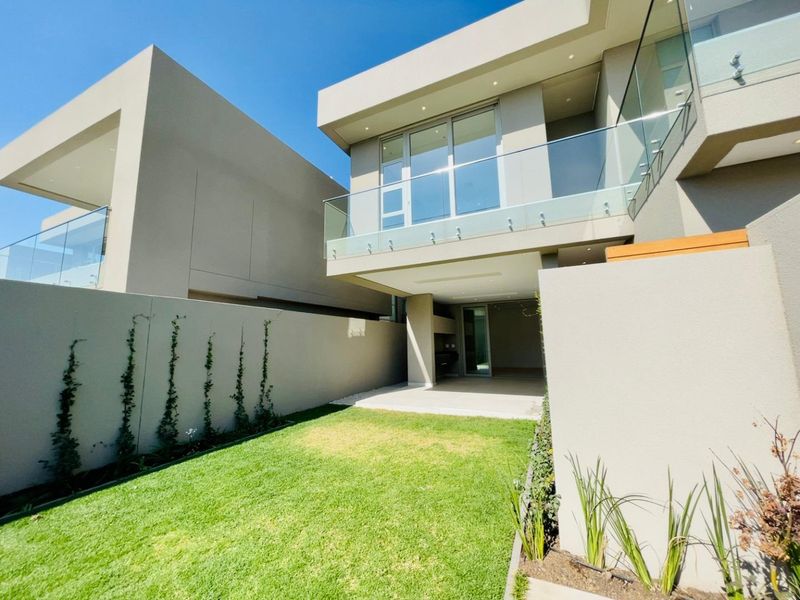 Modern double-story cluster home featuring a private rear garden, covered patio area, and a sleek glass-balustrade balcony on the upper level.
