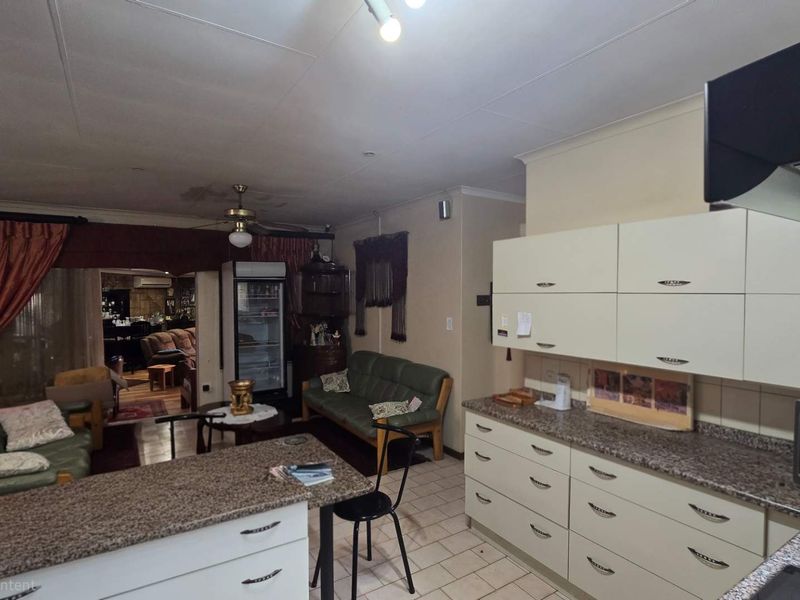 Open-plan kitchen and living area featuring tiled flooring, granite countertops, and built-in cabinetry, with visible ceiling water staining requiring attention.