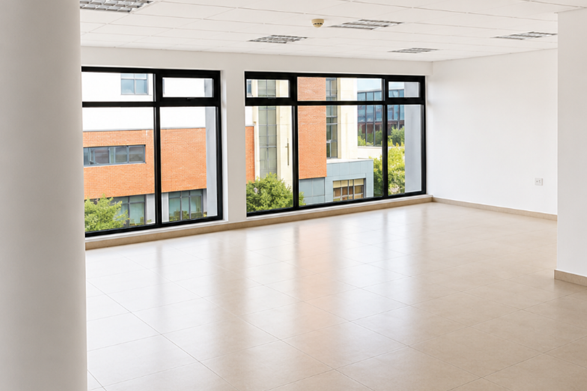 A bright, open-plan office space featuring large windows, neutral ceramic tile flooring, and a professional suspended ceiling with recessed lighting.