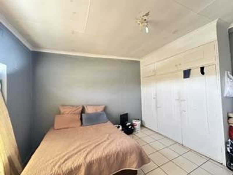 A bedroom featuring built-in cupboards and tiled flooring, requiring cosmetic updates to the ceiling and wall finishes.