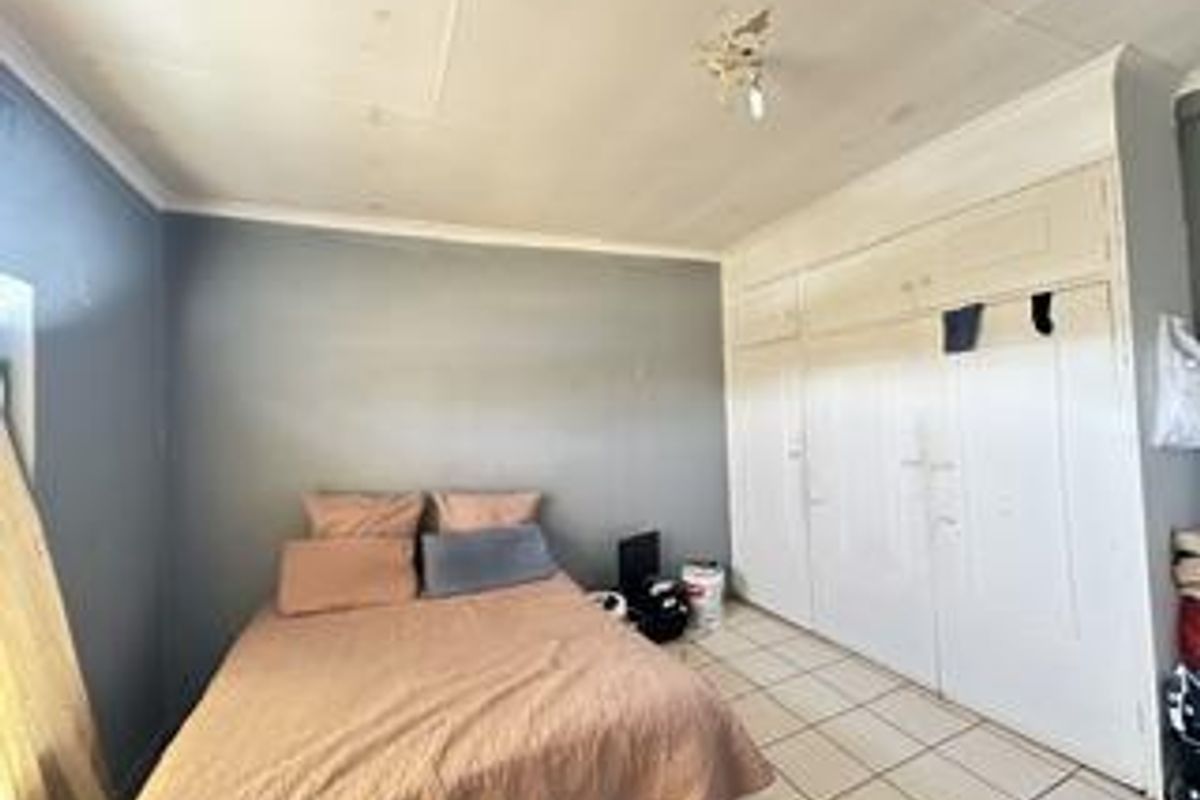 A bedroom featuring built-in cupboards and tiled flooring, requiring cosmetic updates to the ceiling and wall finishes.