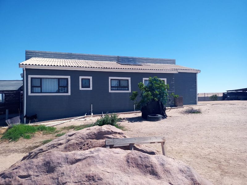 Rear view of a small holding dwelling featuring dark grey exterior walls, aluminium window frames with security bars, and roof-mounted solar panels.