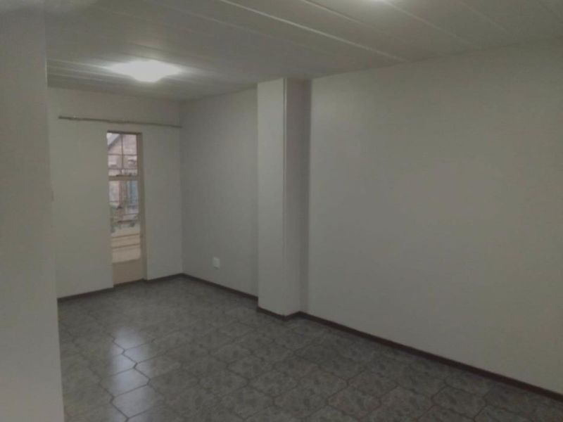 An empty, neutral-toned living area featuring tiled flooring and a simple ceiling finish, providing a blank canvas for interior design.
