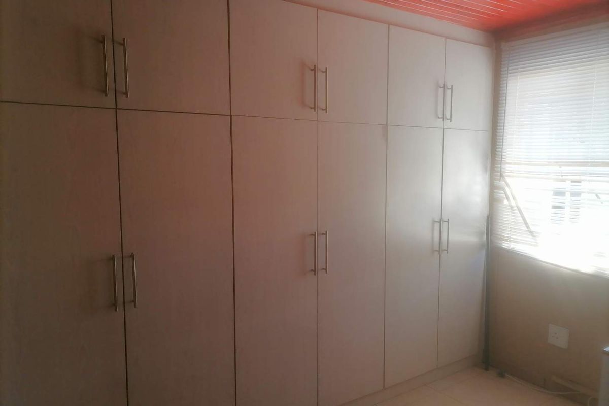A bedroom featuring a large wall-to-wall built-in wardrobe with modern handles and a window with fitted blinds.