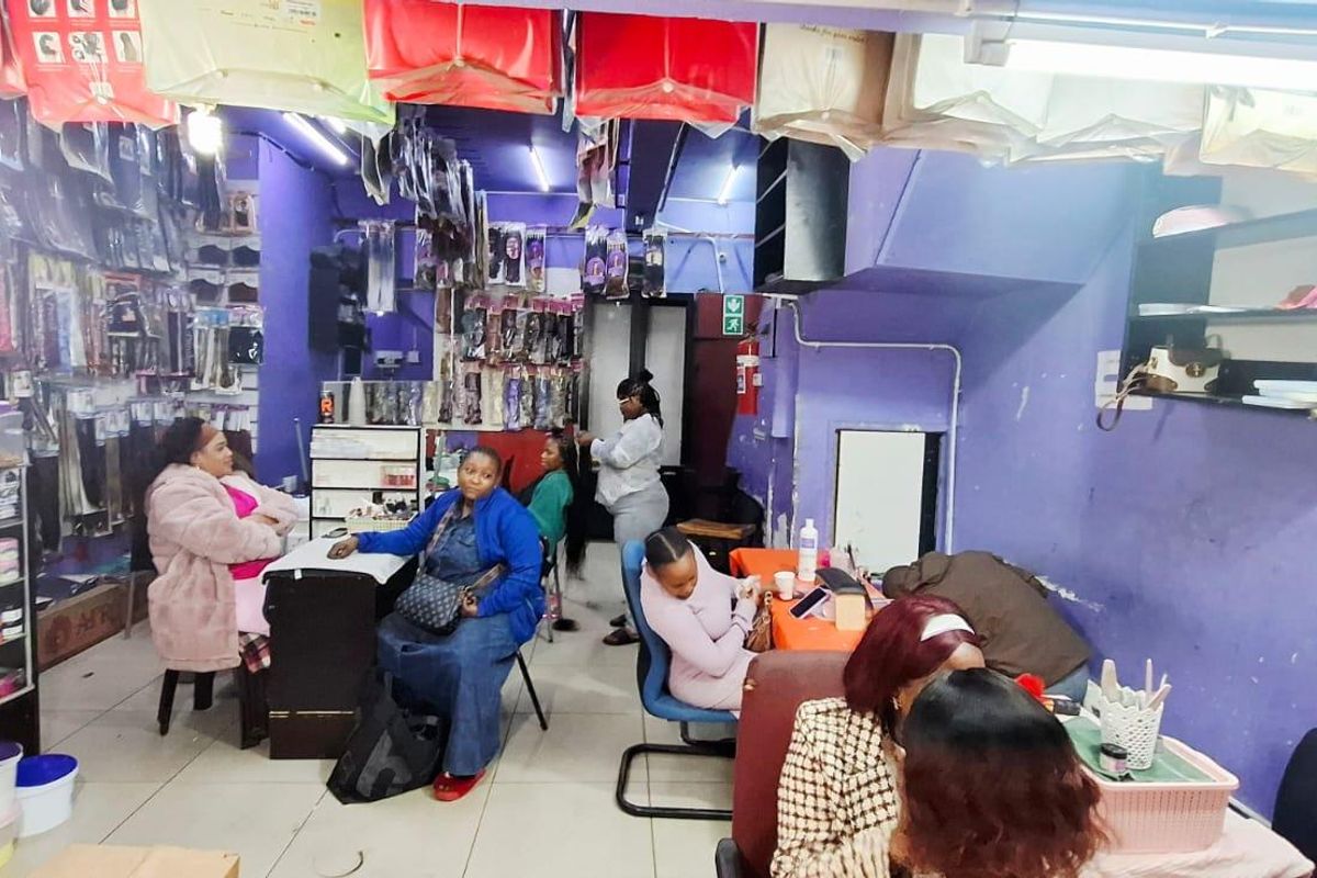 Interior view of a commercial hair salon space featuring tiled flooring, built-in shelving units, and overhead fluorescent lighting.