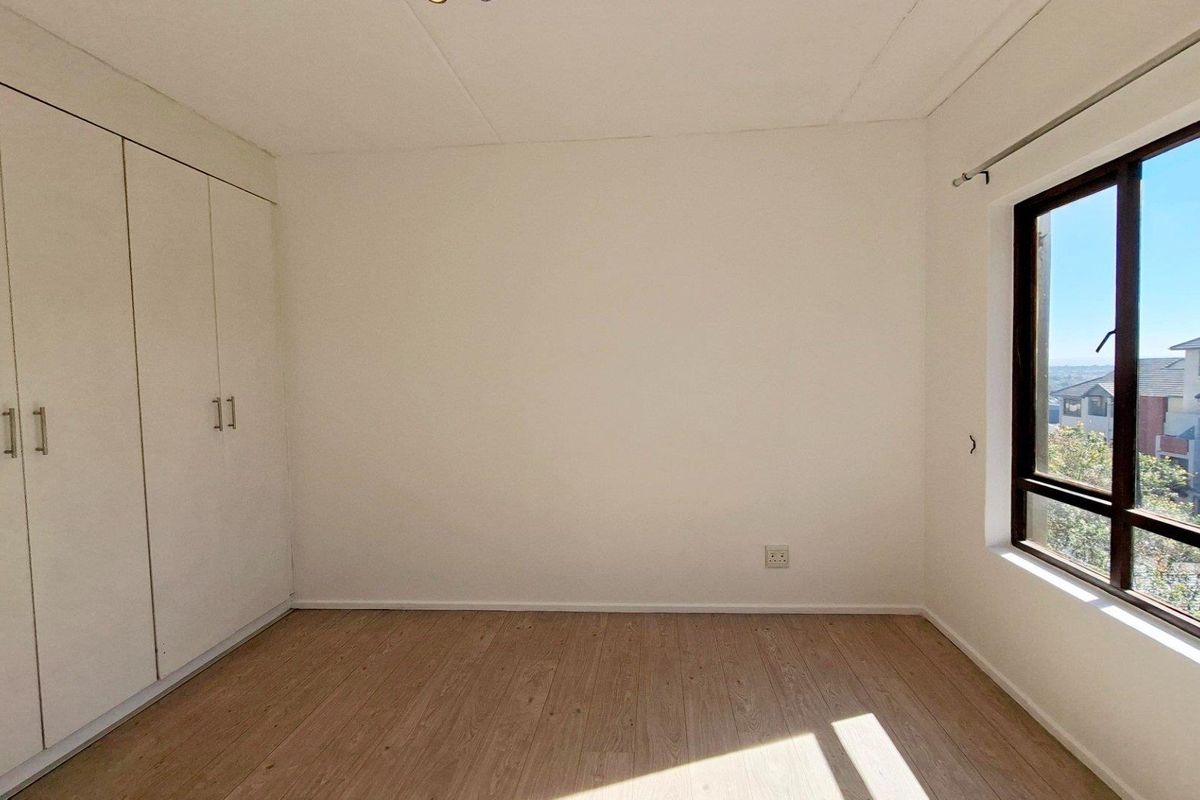 A bright, empty bedroom featuring light-toned laminate flooring and built-in cupboards, offering a clean and neutral space ready for personalization.