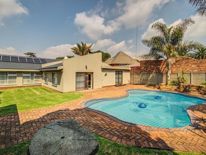 Rear exterior view featuring a swimming pool, brick paved patio area, landscaped lawn, and solar panels installed on the tiled roof.