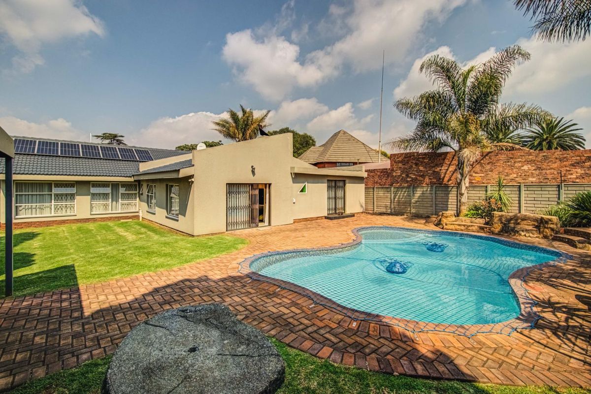 Rear exterior view featuring a swimming pool, brick paved patio area, landscaped lawn, and solar panels installed on the tiled roof.