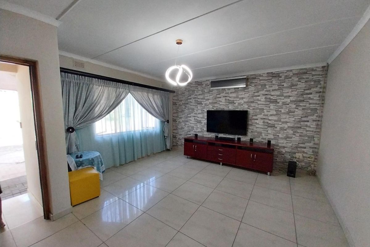 A well-maintained living room featuring tiled flooring, a split-system air conditioner, and a decorative stone-effect feature wall.