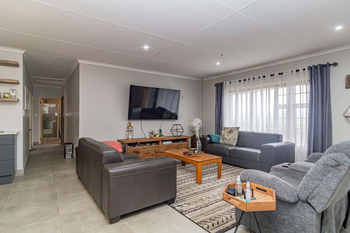 A spacious living room featuring tiled flooring, recessed downlighting, and built-in cabinetry with floating shelves, offering a comfortable and functional living space.