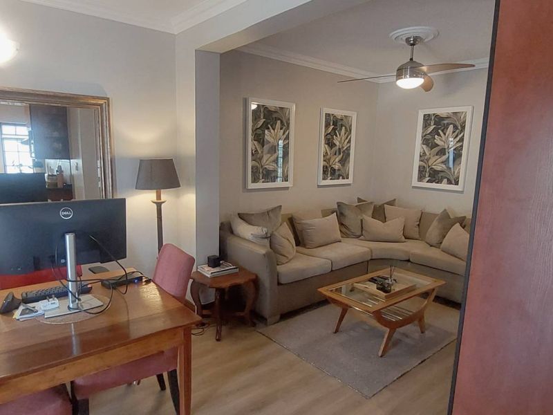 An open-plan living area featuring laminate flooring, a ceiling fan, and coving, creating a comfortable and connected space for relaxation and work.