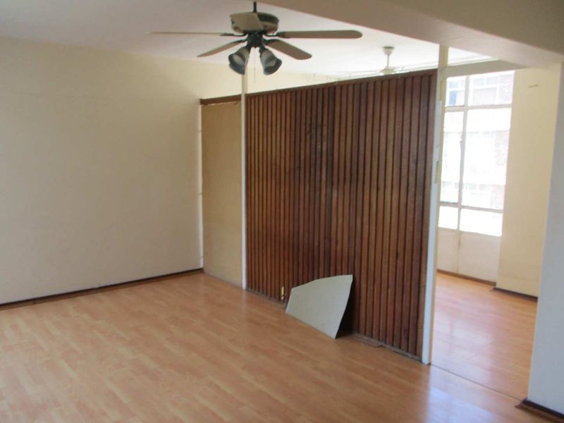 An empty living area featuring laminate flooring, a ceiling fan, and a timber slat room divider with some visible wear.