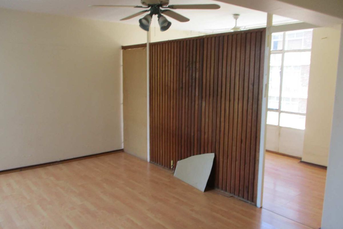 An empty living area featuring laminate flooring, a ceiling fan, and a timber slat room divider with some visible wear.