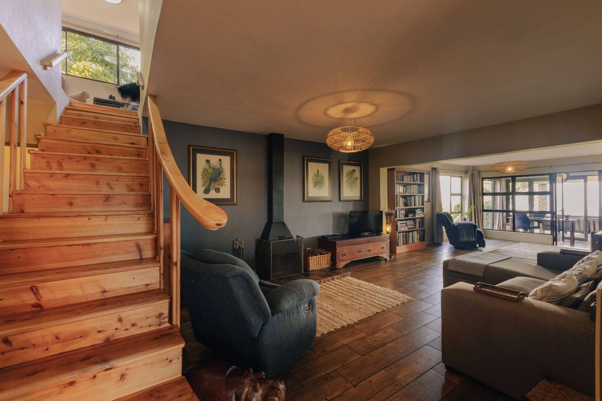 Spacious living room featuring warm timber flooring, a central freestanding fireplace, and a prominent timber staircase leading to the upper level.