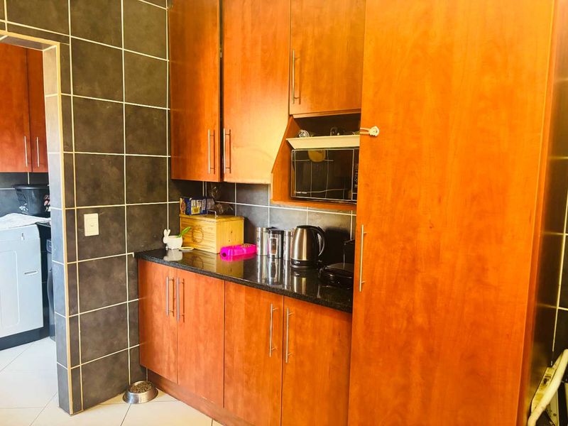 A functional scullery area featuring warm-toned wooden cabinetry, dark granite countertops, and a tiled backsplash, providing additional prep and storage space.