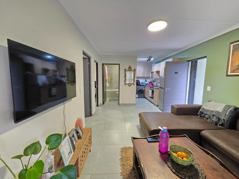 Open-plan living area featuring tiled floors, recessed lighting, and a functional kitchen with built-in cabinetry and appliances, leading to adjacent rooms.