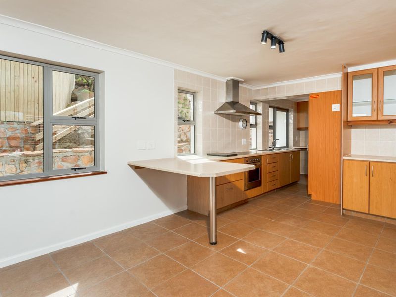 A functional kitchen featuring wooden cabinetry, a built-in oven with extractor fan, tiled backsplash, and a breakfast bar, with ceramic floor tiles throughout.