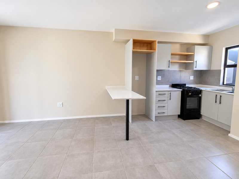 Modern kitchen featuring light grey cabinetry, stone countertops, a breakfast bar, and a built-in gas stove with oven, set against neutral tiled flooring.