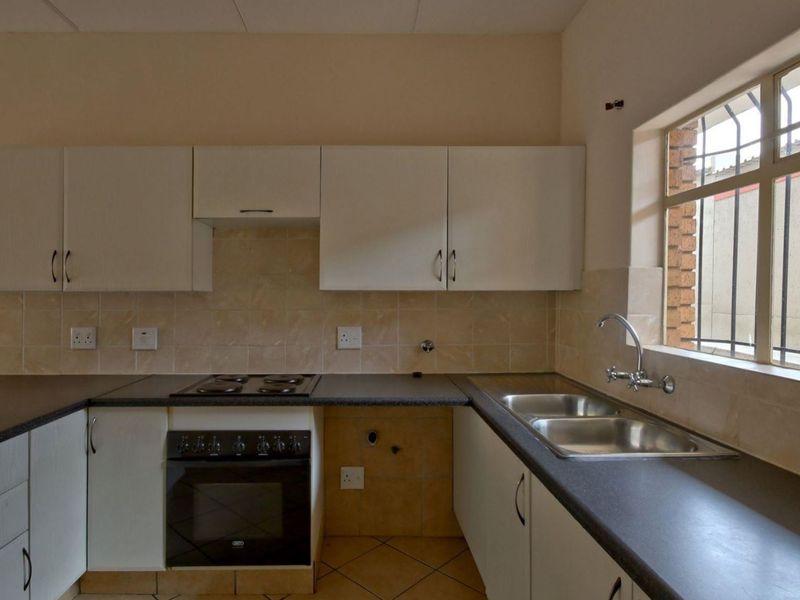 A functional kitchen featuring built-in cabinetry, laminate countertops, an electric hob, oven, and a double bowl stainless steel sink with tiled backsplash.
