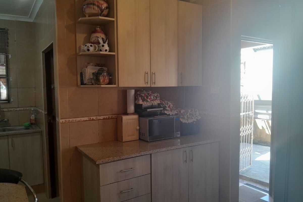 A functional kitchen area featuring light wood-finish cabinetry, granite countertops, and full-height wall tiling, with direct access to an outdoor patio area.