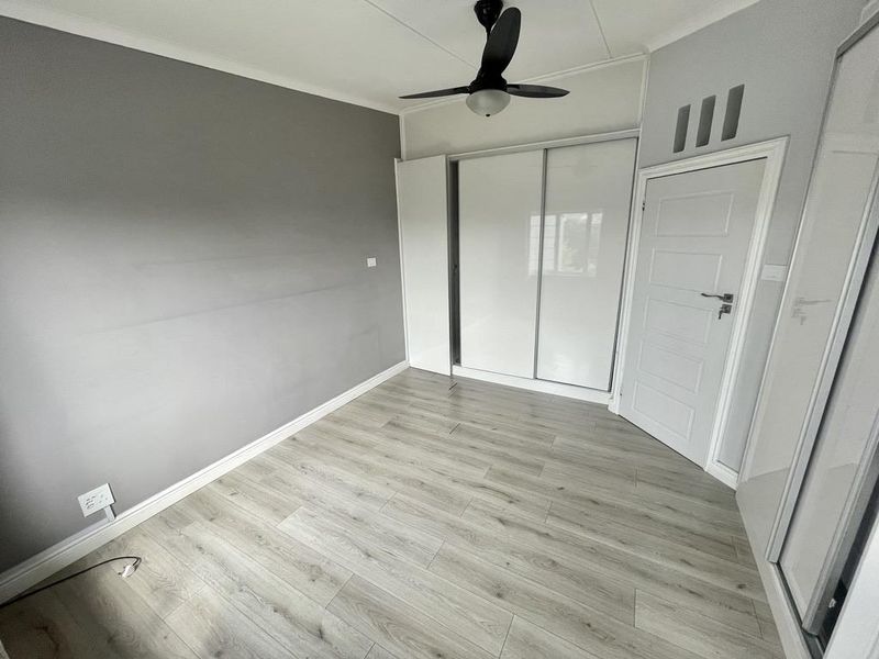 A clean, empty bedroom featuring modern laminate flooring, a built-in sliding wardrobe, and a ceiling fan.