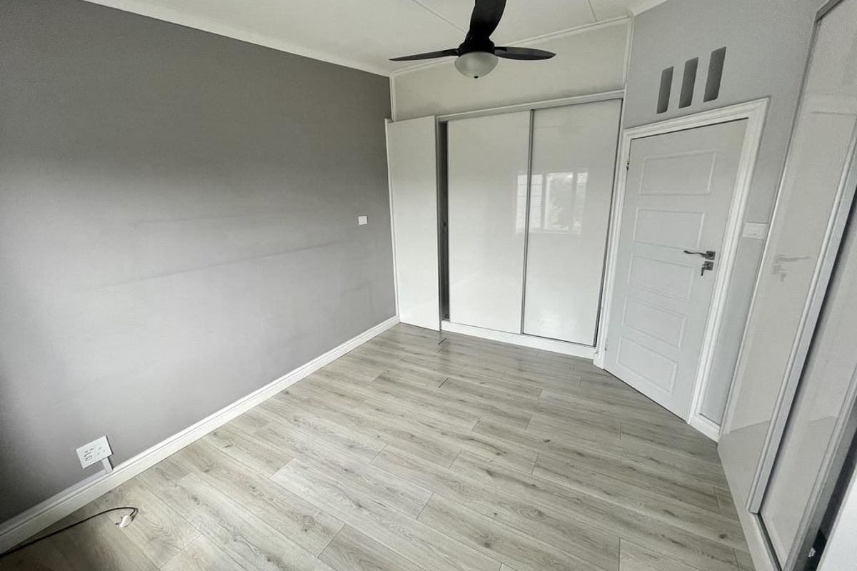 A clean, empty bedroom featuring modern laminate flooring, a built-in sliding wardrobe, and a ceiling fan.