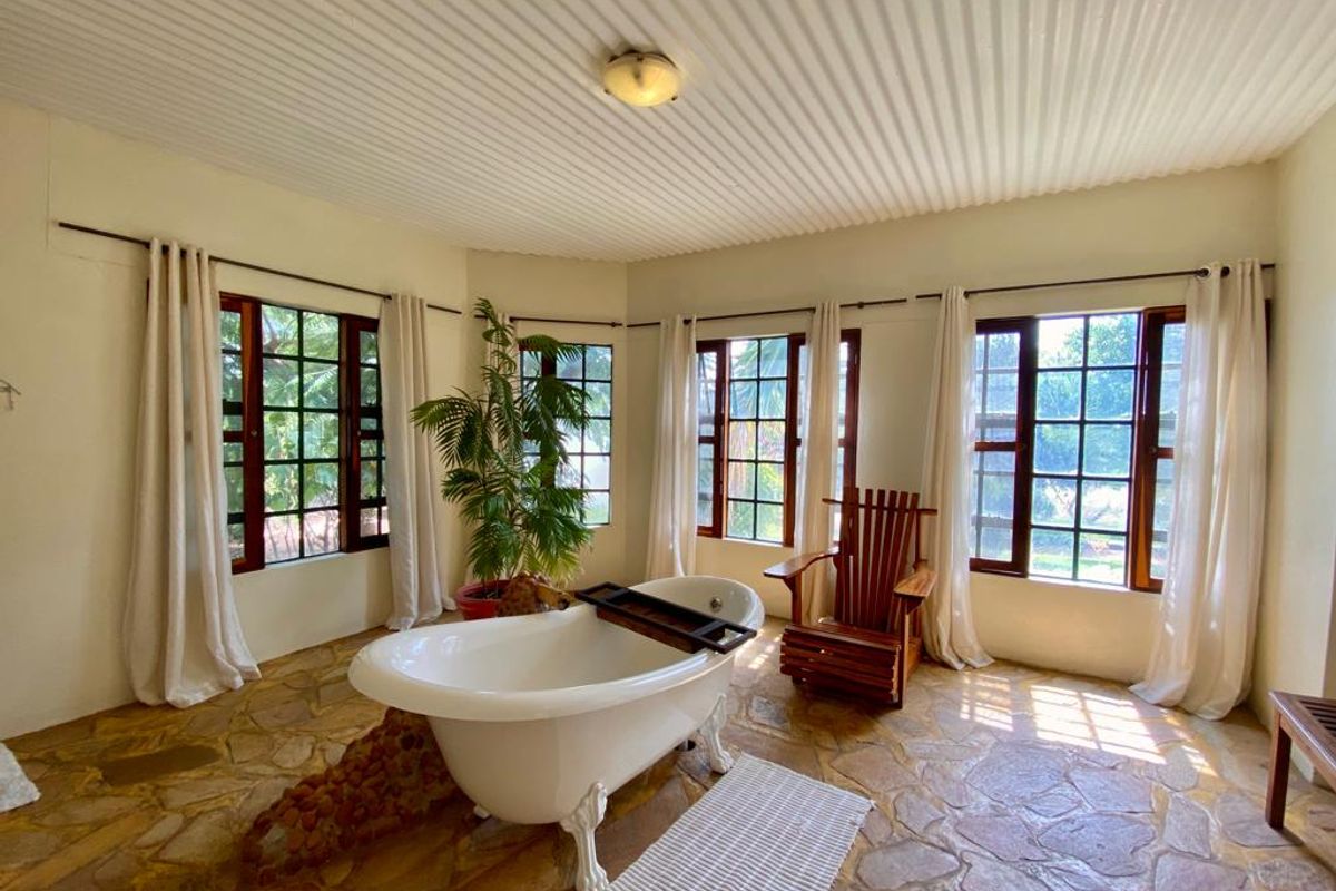 A bright and airy bathroom featuring a classic clawfoot bathtub, natural stone flooring, and large grid-pattern windows that provide ample natural light.