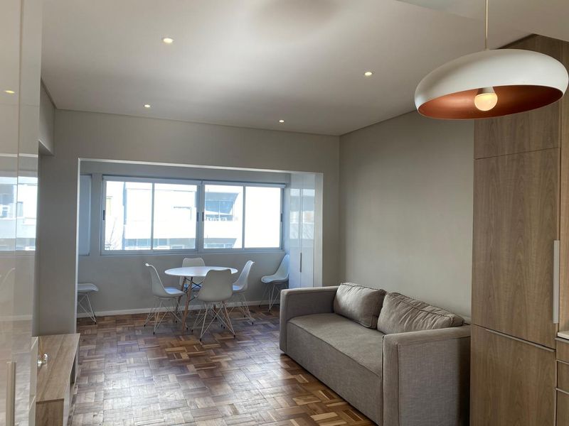 Modern open-plan living and dining area featuring classic parquet flooring, recessed lighting, and neutral wall finishes with ample natural light.