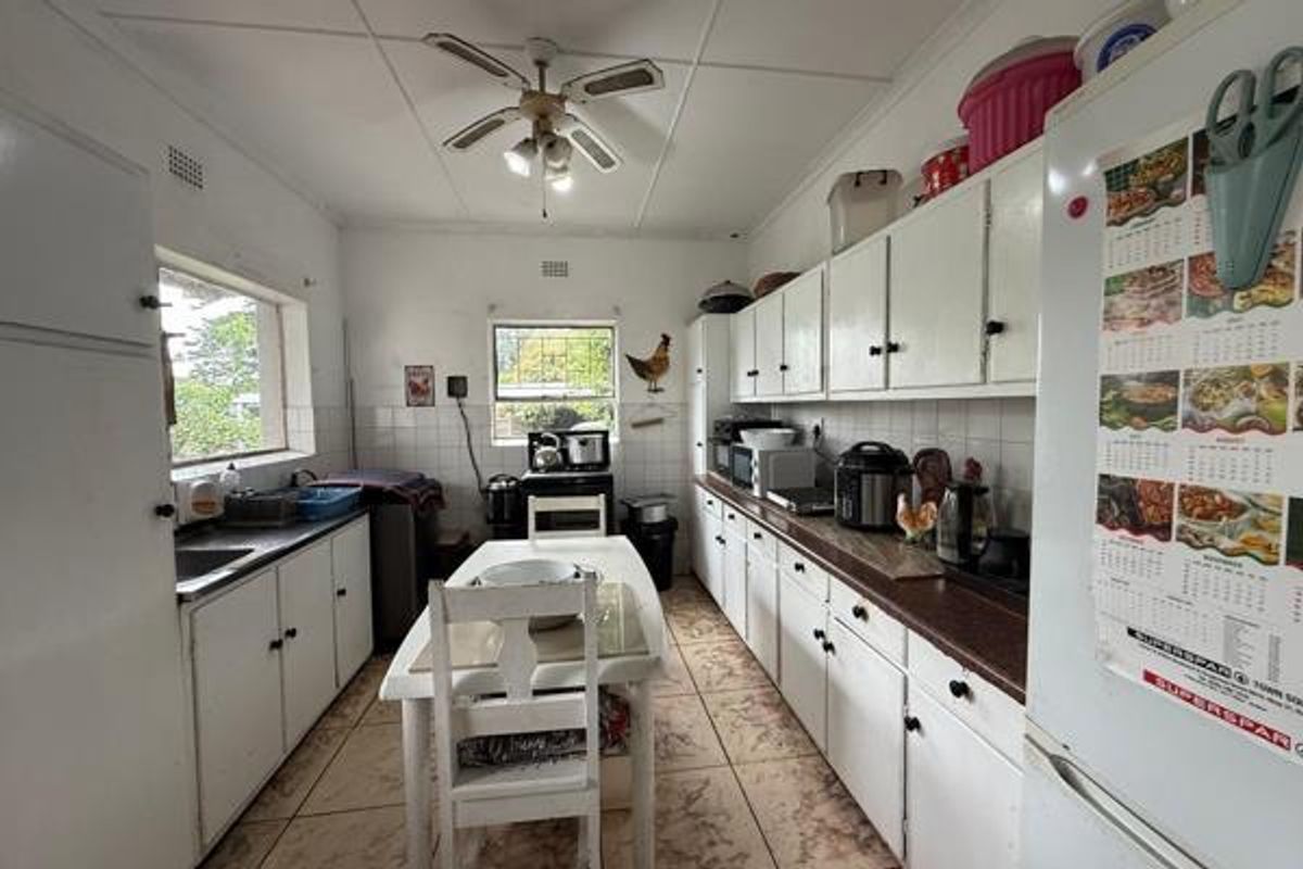 A functional kitchen featuring white cabinetry, tiled countertops, and a central dining area, offering a practical layout with ample storage space.