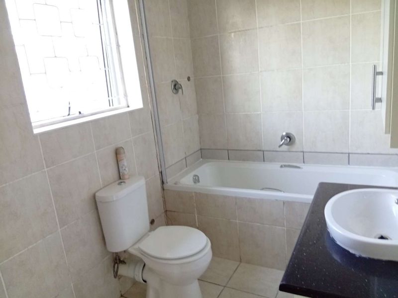 A functional bathroom featuring a built-in bathtub, toilet, and vanity basin with tiled finishes throughout.
