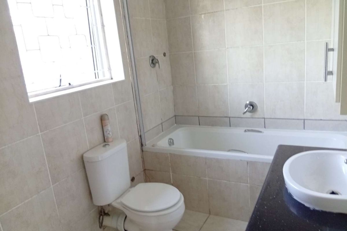 A functional bathroom featuring a built-in bathtub, toilet, and vanity basin with tiled finishes throughout.