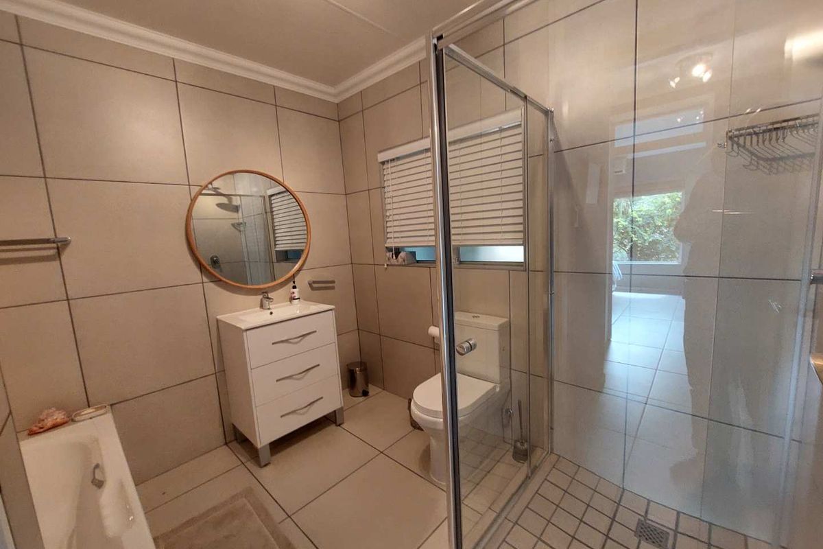 Modern bathroom featuring a glass-enclosed shower, built-in bathtub, vanity cabinet with basin, and neutral floor-to-ceiling tiling.