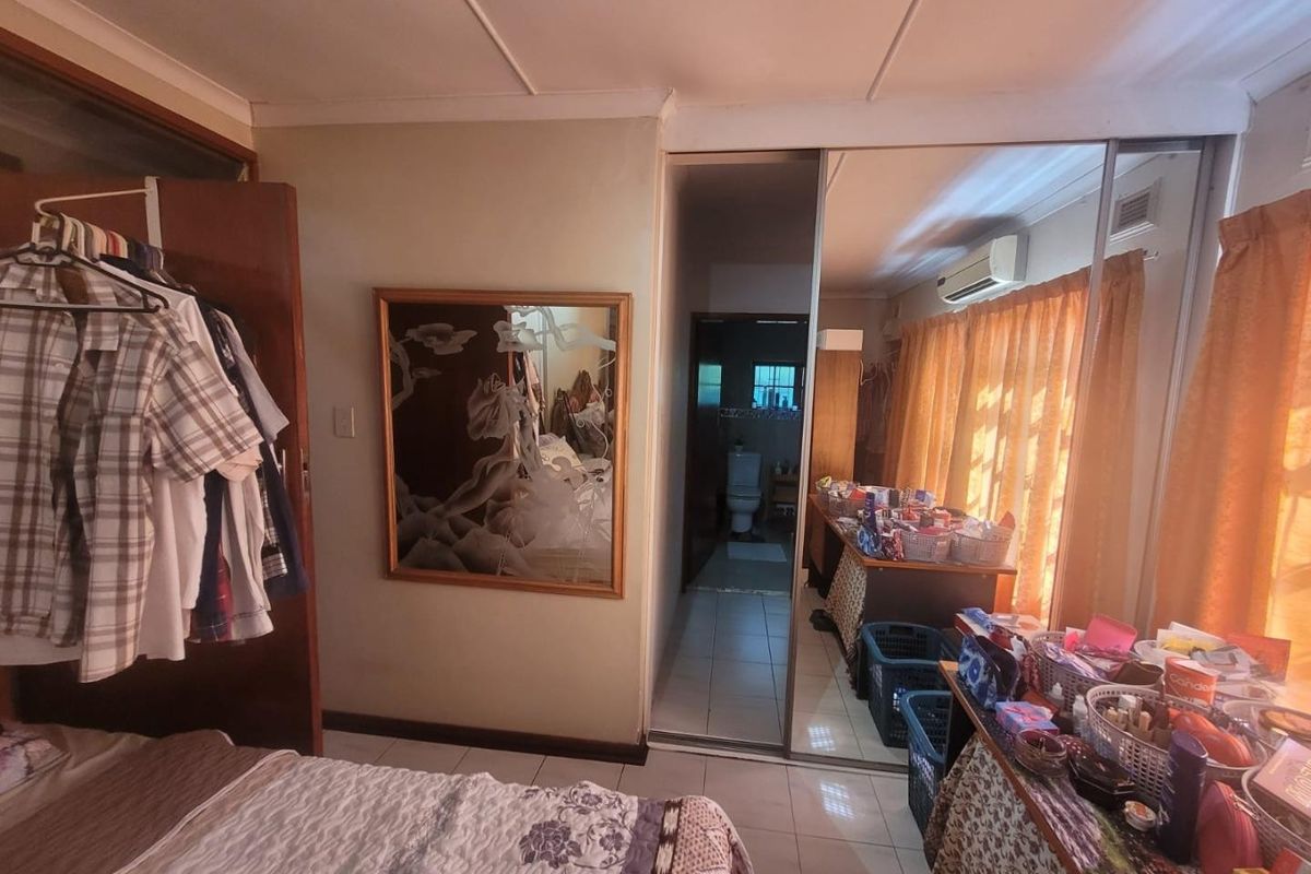 A bedroom featuring tiled flooring, a split-system air conditioner, and built-in mirrored sliding wardrobes with direct access to an en-suite bathroom.