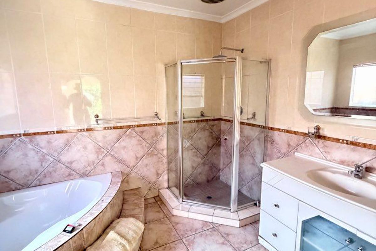 A functional bathroom featuring a corner bathtub, separate shower enclosure, and a vanity unit with integrated sink and wall mirror.